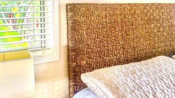 A bedroom with a bed, a nightstand, a window with blinds, and a framed picture on the wall.