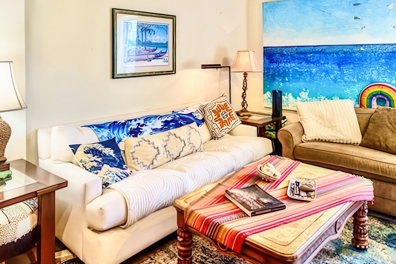 A living room with a sofa, a coffee table, and a painting of a beach scene.