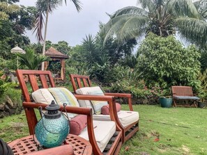 Um jardim com duas cadeiras de madeira, um candeeiro e um gazebo.