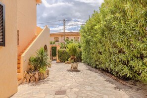 A paved courtyard with a stone pathway, a staircase, and a large hedge on one side. - Appartamento Delle Rose by Wonderful Italy (Budoni)