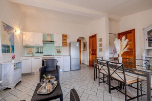 A modern kitchen with white cabinets, a dining area with a glass table, and a refrigerator. - Appartamento Delle Rose by Wonderful Italy (Budoni)