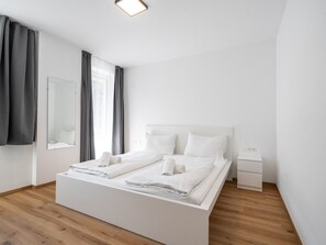 A modern, minimalist bedroom with a large bed, a bedside table, and a mirror.