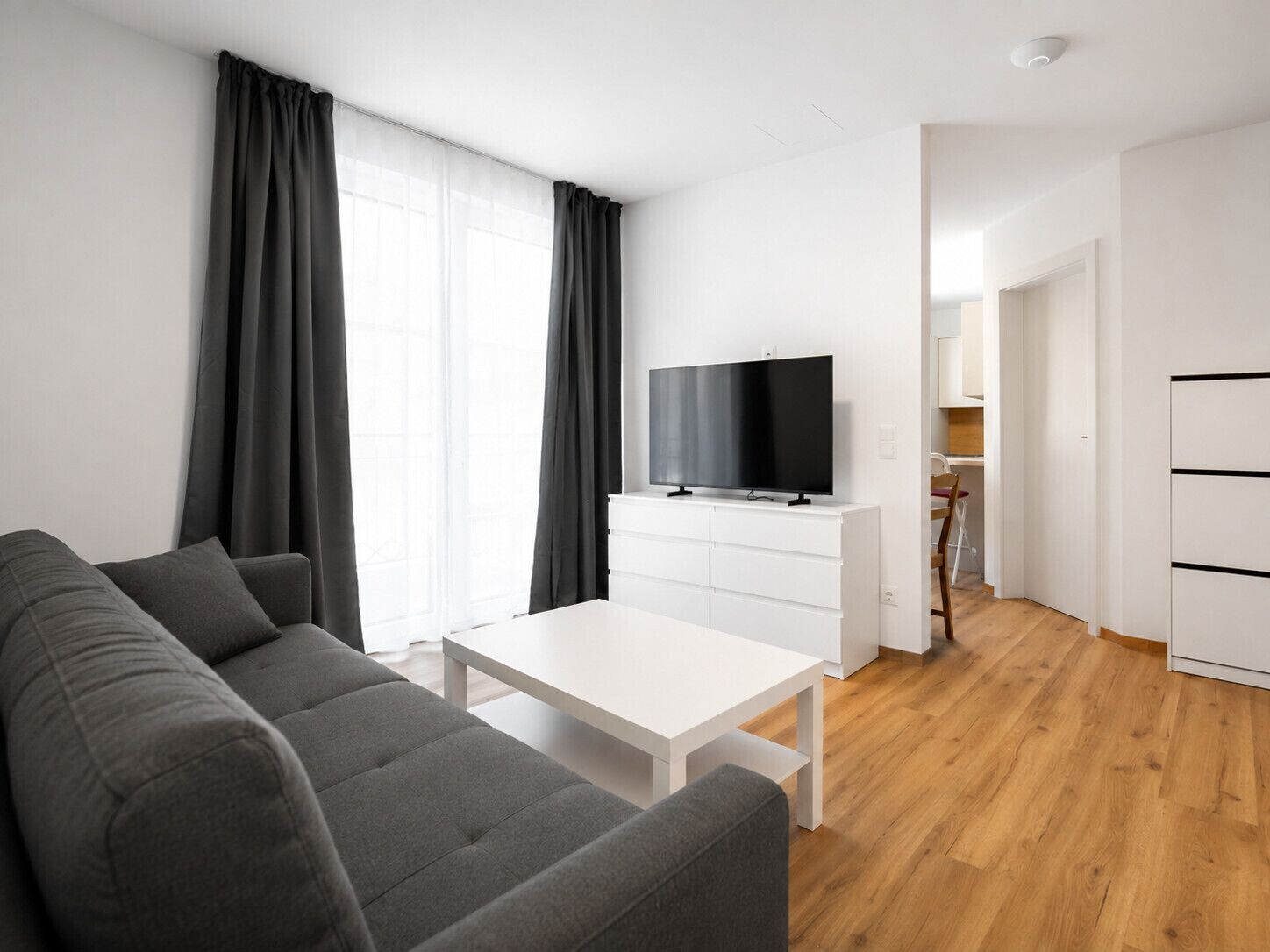 Un salon moderne avec un canapé gris, une table basse blanche et un téléviseur à écran plat posé sur un meuble blanc.