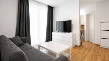 Un salon moderne avec un canapé gris, une table basse blanche et un téléviseur à écran plat posé sur un meuble blanc.