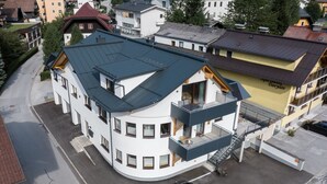 A multi-story building with a curved facade, a balcony, and a parking area with two cars. - Haus3310 - Top 2, Balcony & Central (Bad Hofgastein)