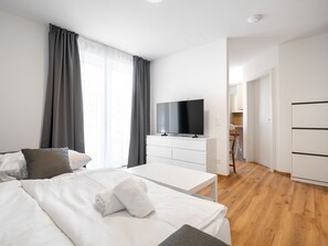 Ein modernes Hotelzimmer mit einem Bett, einem Flachbildfernseher, einer weißen Kommode und Holzboden.
