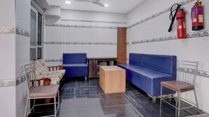 A room with a ceiling fan, two blue sofas, a wooden table, and two chairs. - MG Road Crossway Formerly Ravi Palace (Rajkot)