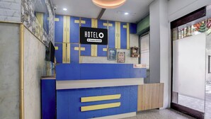 A hotel reception desk with a blue and yellow color scheme, a sign indicating it's company-serviced, and a framed picture above the desk. - MG Road Crossway Formerly Ravi Palace (Rajkot)