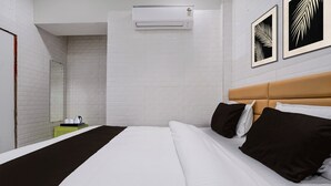 A hotel room with a bed, a bedside table, a mirror, and a wall-mounted air conditioner. - MG Road Crossway Formerly Ravi Palace (Rajkot)