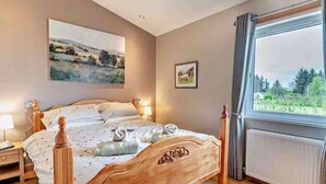 Quarto com cama de madeira, um quadro na parede e janela com vista para áreas verdes.