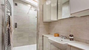 Uma casa de banho moderna com cabine de duche em vidro, lavatório com espelho e barra de toalhas.