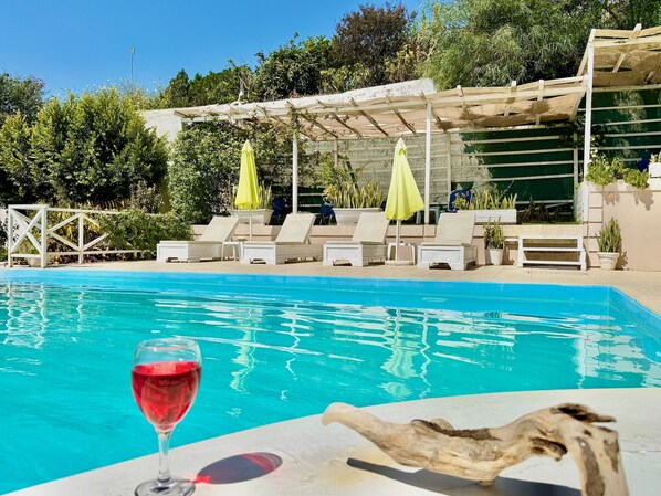 A pool with lounge chairs and umbrellas, surrounded by greenery.