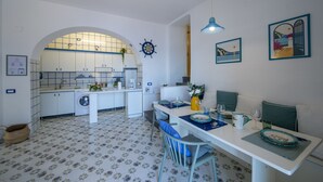 Une cuisine compacte équipée d’un lave-linge, un coin repas avec une table pour deux personnes et un petit espace salon.