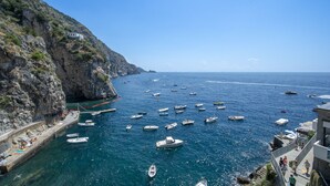 Une zone côtière où de nombreux bateaux sont amarrés le long de la rive, avec une falaise rocheuse et un ciel bleu dégagé.