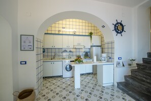 A compact kitchen with white cabinets, a washing machine, and a coffee maker. - Casa Albachiara | Waterfront, Just Steps from the Beach (Praiano)