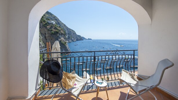 Un balcon avec vue sur la mer, une chaise, un chapeau et un sac.