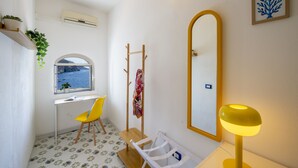Une petite salle de bain avec une fenêtre, un miroir, une chaise jaune, une petite table et une plante.