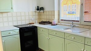 A kitchen with a black stove, a sink, and light green cabinets. - Grays Cosy 1-Bed Apartment Sleeps 4 near Station (Grays)
