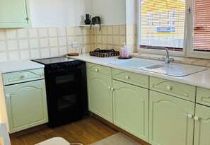 A kitchen with a black stove, a sink, and light green cabinets. - Grays Cosy 1-Bed Apartment Sleeps 4 near Station (Grays)