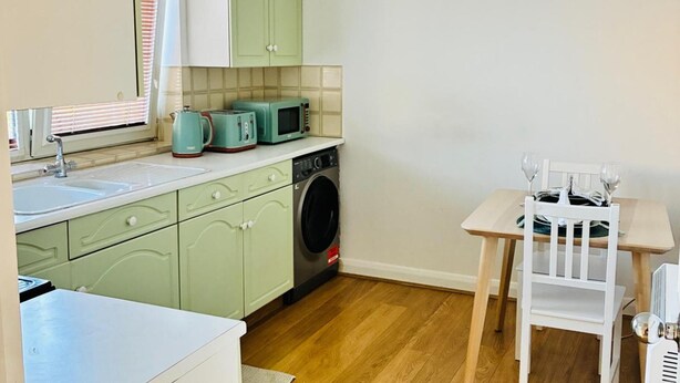 A compact kitchen with a washing machine, a sink, and a dining area with a table and chairs. - Grays Cosy 1-Bed Apartment Sleeps 4 near Station (Grays)
