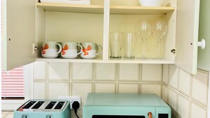 A kitchen with a teal toaster, a white cabinet with a bowl and glasses, and a window with blinds. - Grays Cosy 1-Bed Apartment Sleeps 4 near Station (Grays)