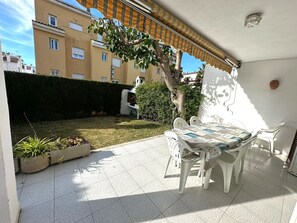 Een terras buiten met een tafel en stoelen, een betegelde vloer en een gebouw op de achtergrond.