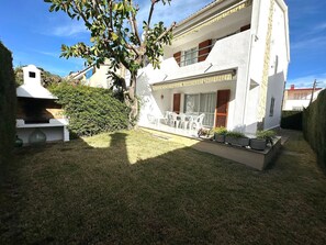Una casa a due piani con patio, barbecue e un piccolo giardino.