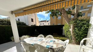 Une terrasse extérieure avec une table ronde et des chaises, un auvent à rayures et une vue sur les bâtiments en arrière-plan.