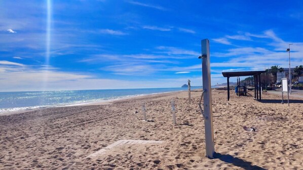 A beach with a clear sky, a sandy shore, and a structure with a roof.
