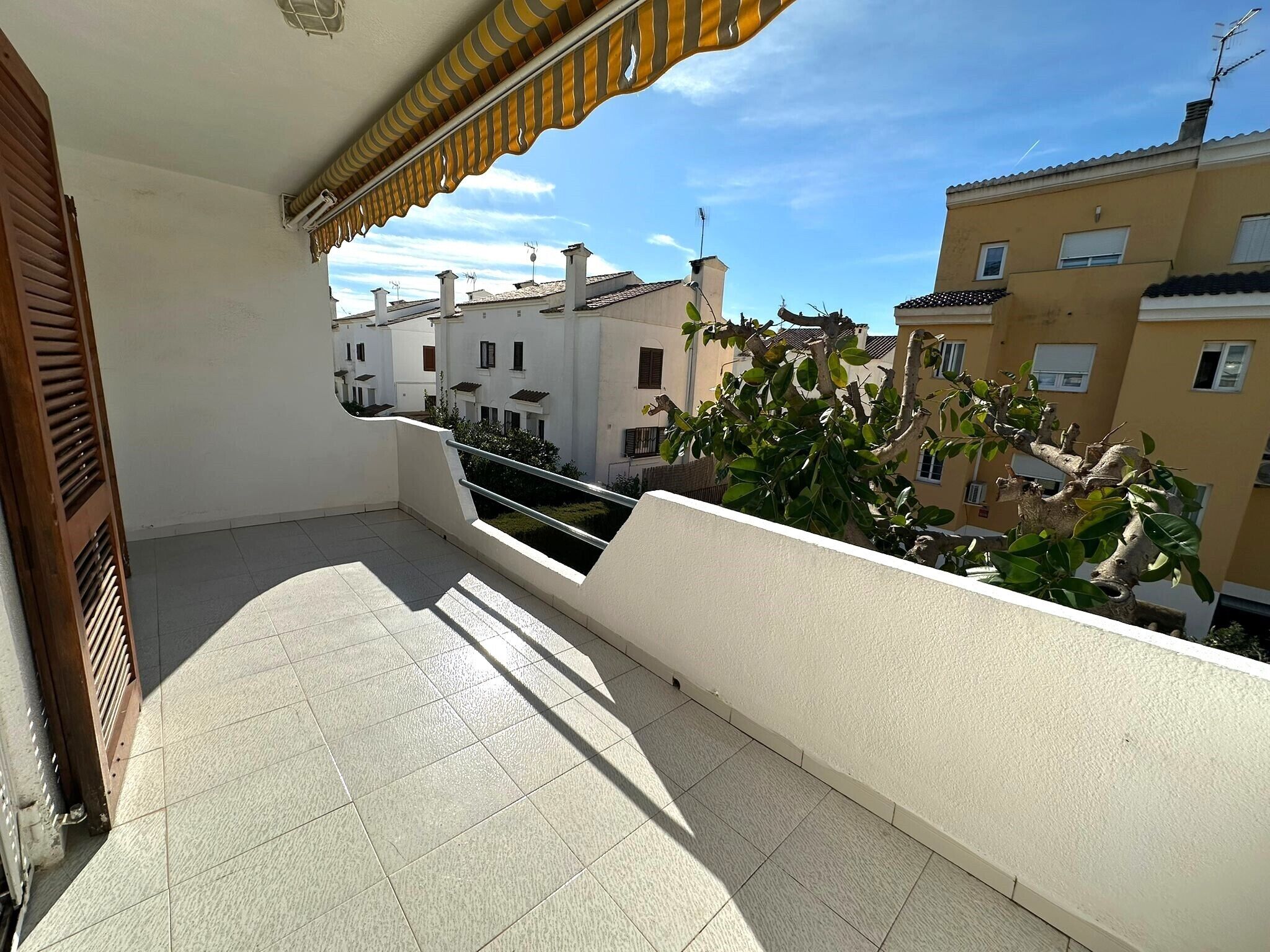 Un balcon doté d’un sol carrelé, d’une rambarde en métal et offrant une vue sur les bâtiments voisins.