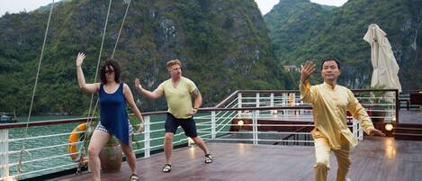 A group of people performing on a wooden deck with a view of green mountains in the background.