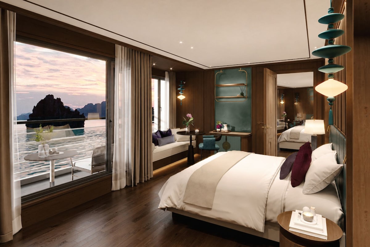A modern hotel room with a large bed, a small table, a nightstand, and a view of a body of water.