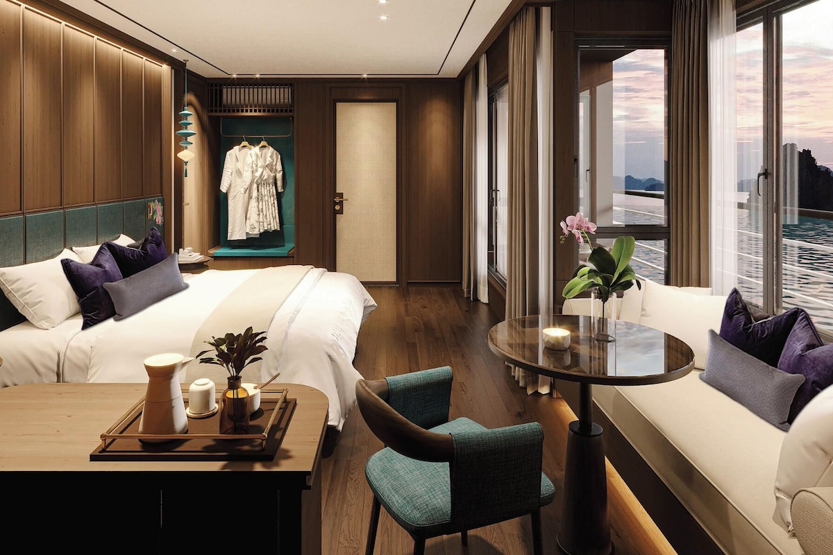 A hotel room with a bed, a dining table with a tray, a sofa, and a view of the water.