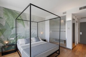 Ein modernes Schlafzimmer mit einem Himmelbett aus Glas, einem Nachttisch mit Lampe sowie einer Wand mit einem tropischen Blatt-Wandgemälde.