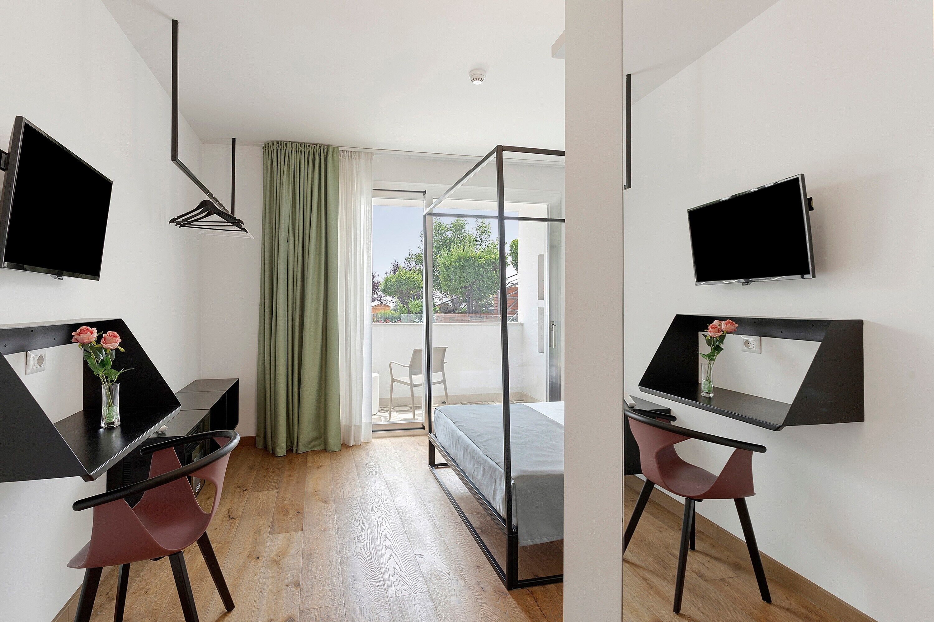 A modern room with a bed, two desks with computers, a TV, and a window with curtains.