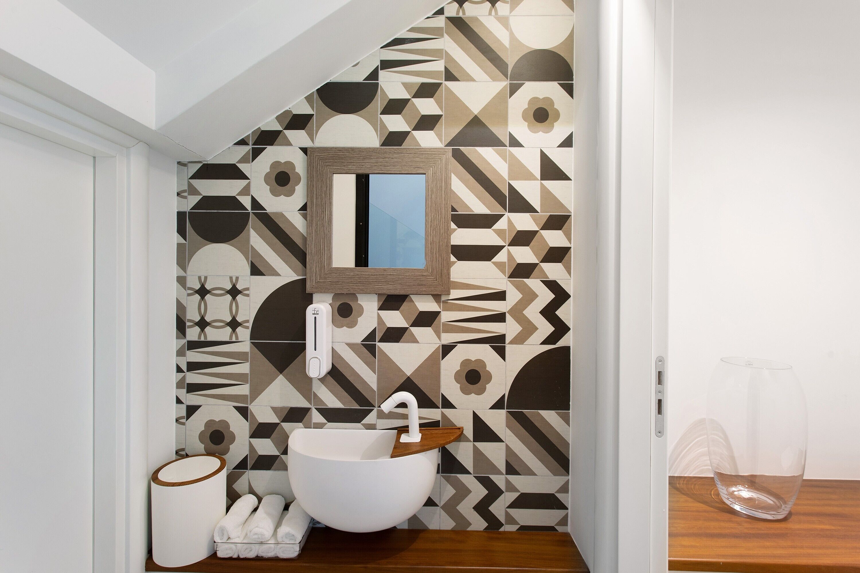 A bathroom with a geometric patterned wall, a white sink, and a wooden vanity.