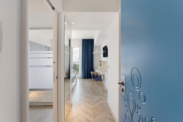 A modern hotel room with a wooden floor, a bed, a desk, and a view of the outdoors.