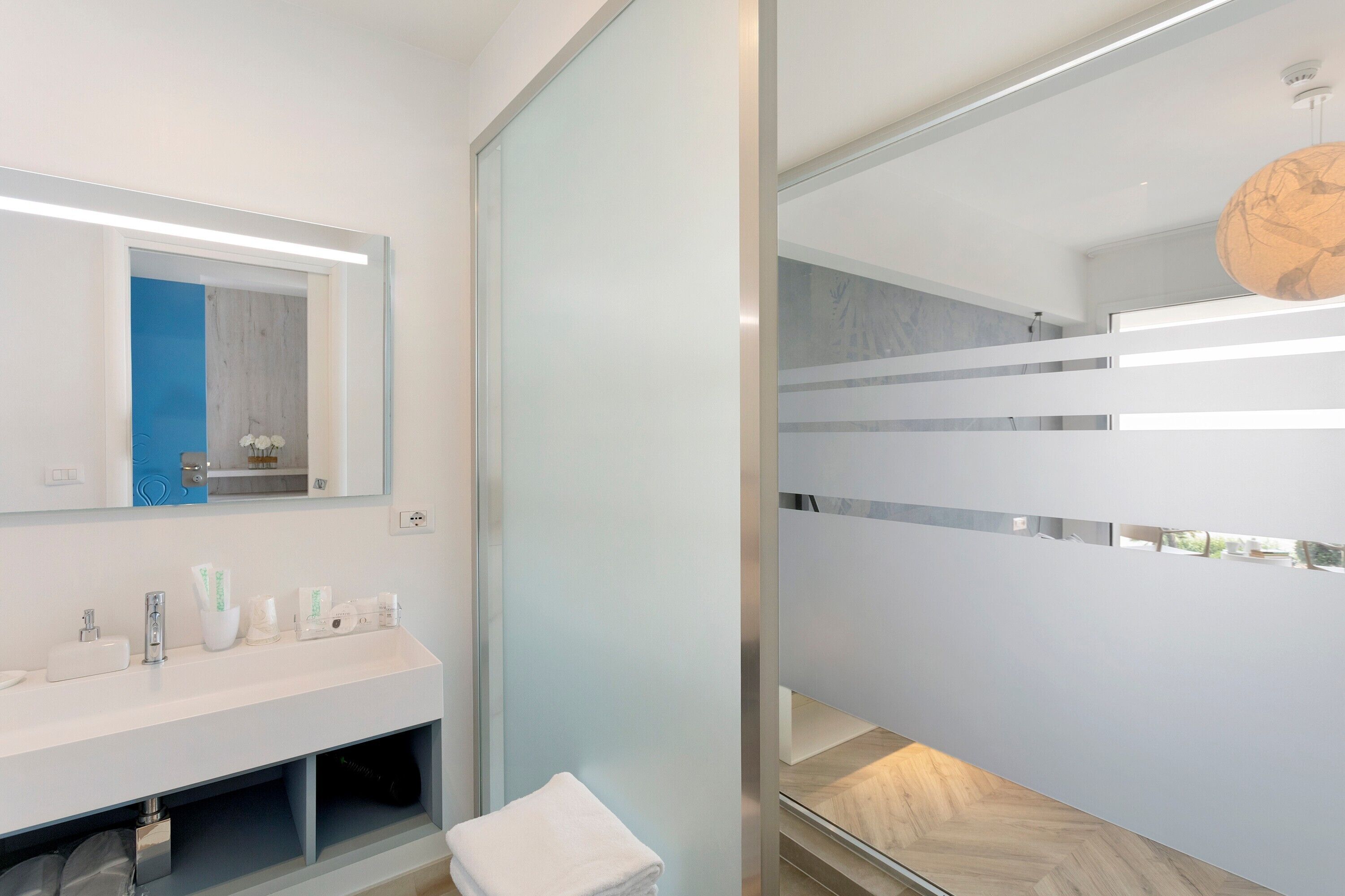 Un baño moderno con tocador blanco, espejo y mampara de vidrio.