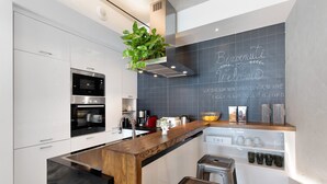 A modern kitchen with white cabinetry, a stainless steel range hood, a wooden island, and a chalkboard wall with writing. - 'Haddar Etna' – Sapphire (Zafferana Etnea)