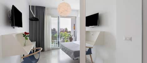 Habitación de hotel moderna con cama, escritorio, silla, televisor y vistas al exterior.