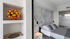 Een moderne slaapkamer met een bed, een hoofdeinde met marmerprint, een bloemstuk op een plank en een wandlamp.