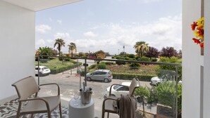 Een balkon met twee stoelen, een tafel met een wijnglas en uitzicht op een parkeerplaats met auto's en groen.