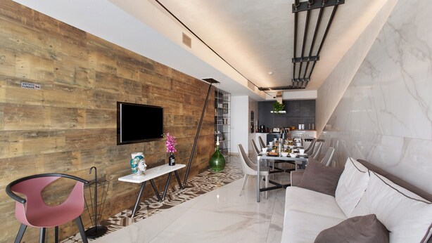 Een moderne woonkamer met een houten accentmuur, een flatscreen televisie, een eethoek met een tafel en stoelen, en een bank.