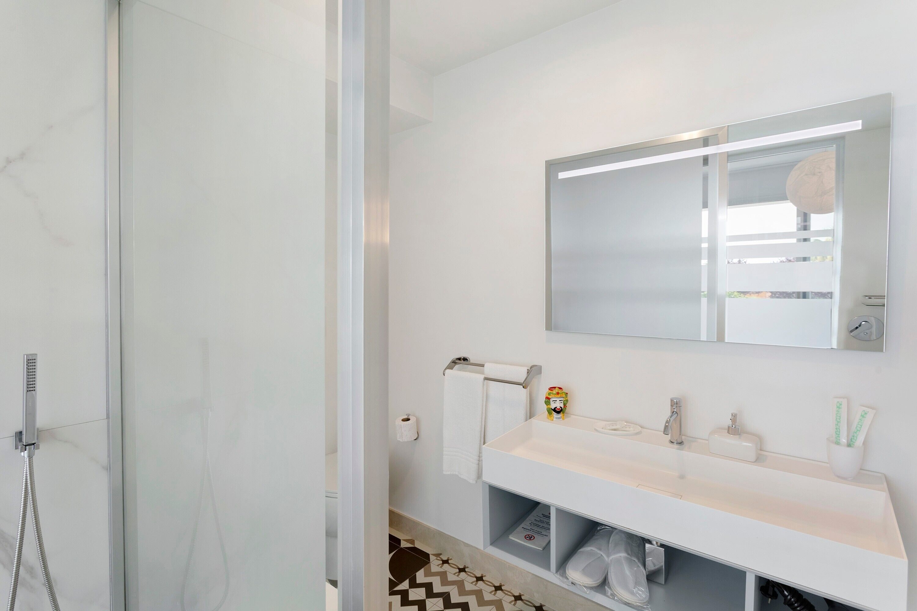 Un bagno moderno con box doccia in vetro, un mobile lavabo bianco con specchio e un porta asciugamani.
