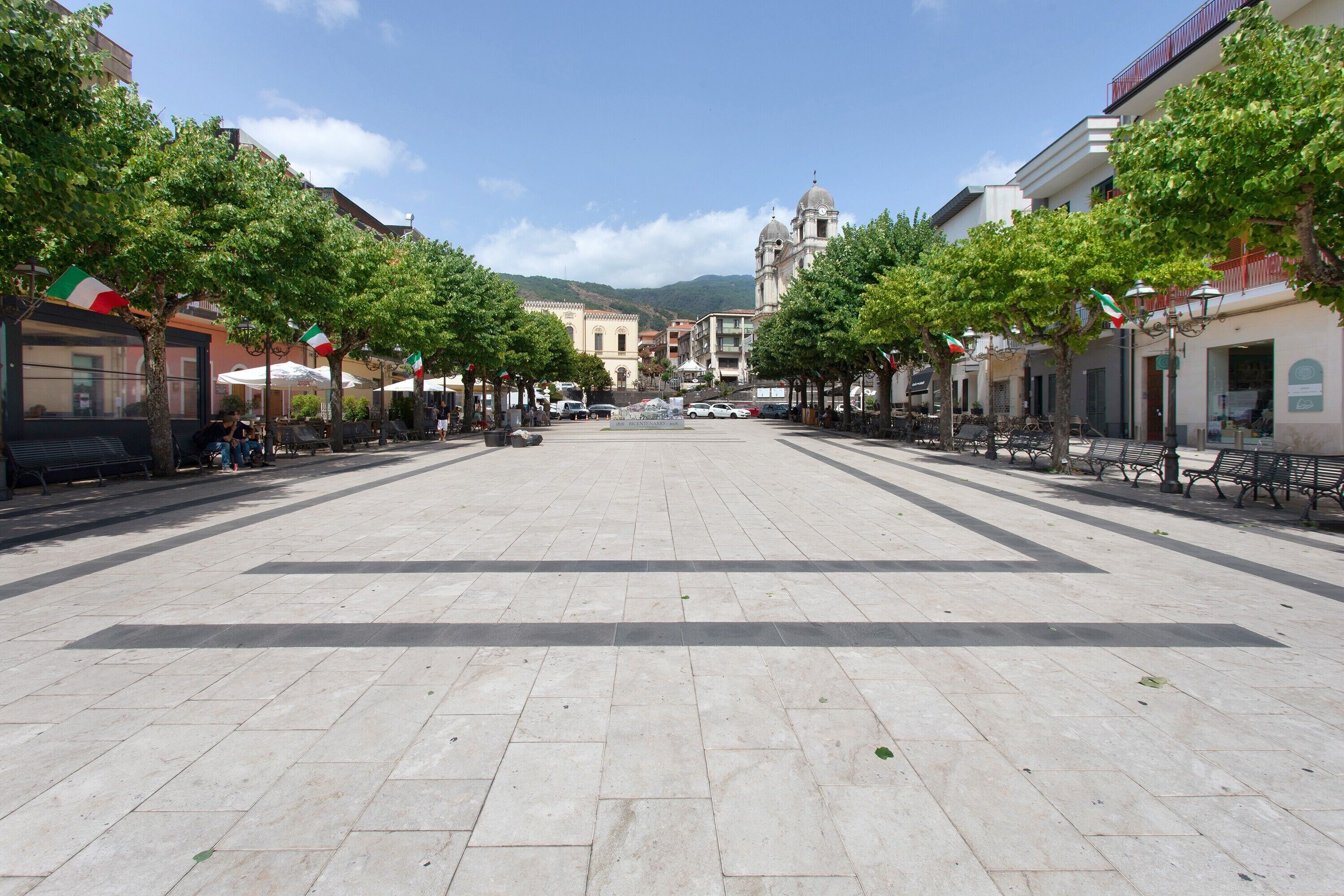 A spacious public square with a central open area, flanked by trees and buildings.
