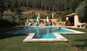 A rectangular swimming pool with a stone border, surrounded by grass, with outdoor seating and umbrellas. - Lodge in the heart of a vineyard in Provence – Cassis and the sea are less than 10 minutes away (Roquefort-la-Bédoule)