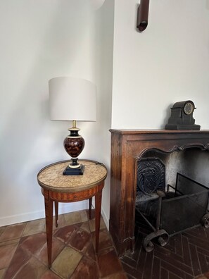 A corner room with a wooden table, a lamp, a fireplace, and a clock. - Lodge in the heart of a vineyard in Provence – Cassis and the sea are less than 10 minutes away (Roquefort-la-Bédoule)