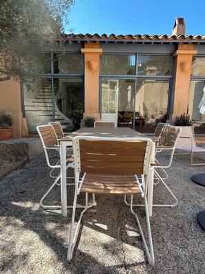 An outdoor patio with a round table and six chairs, a stone wall, and a building with large windows in the background. - Lodge in the heart of a vineyard in Provence – Cassis and the sea are less than 10 minutes away (Roquefort-la-Bédoule)