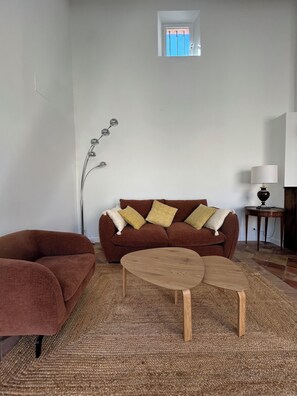 A living room with a brown sofa, two round wooden tables, a floor lamp, and a small window with a view. - Lodge in the heart of a vineyard in Provence – Cassis and the sea are less than 10 minutes away (Roquefort-la-Bédoule)