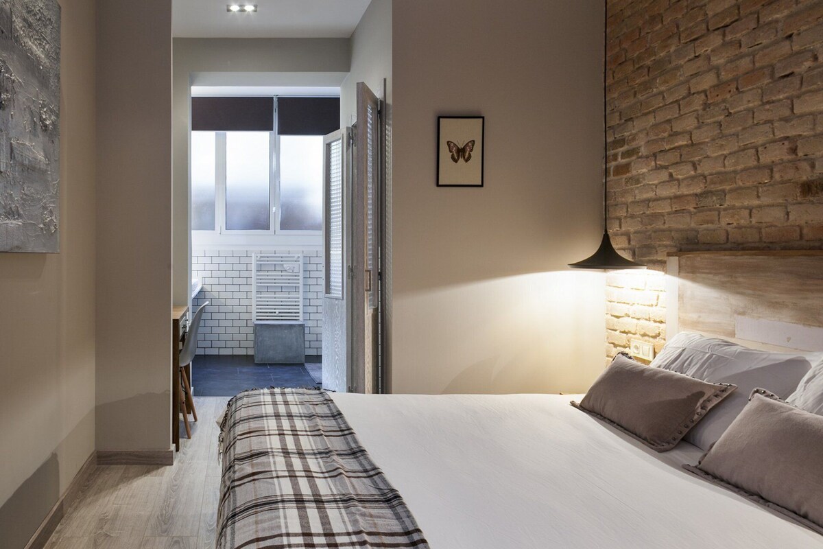 Ein Hotelzimmer mit einem Bett, einer Nachttischlampe, einem Schmetterlingsbild und Blick auf ein Badezimmer mit Handtuchhalter.